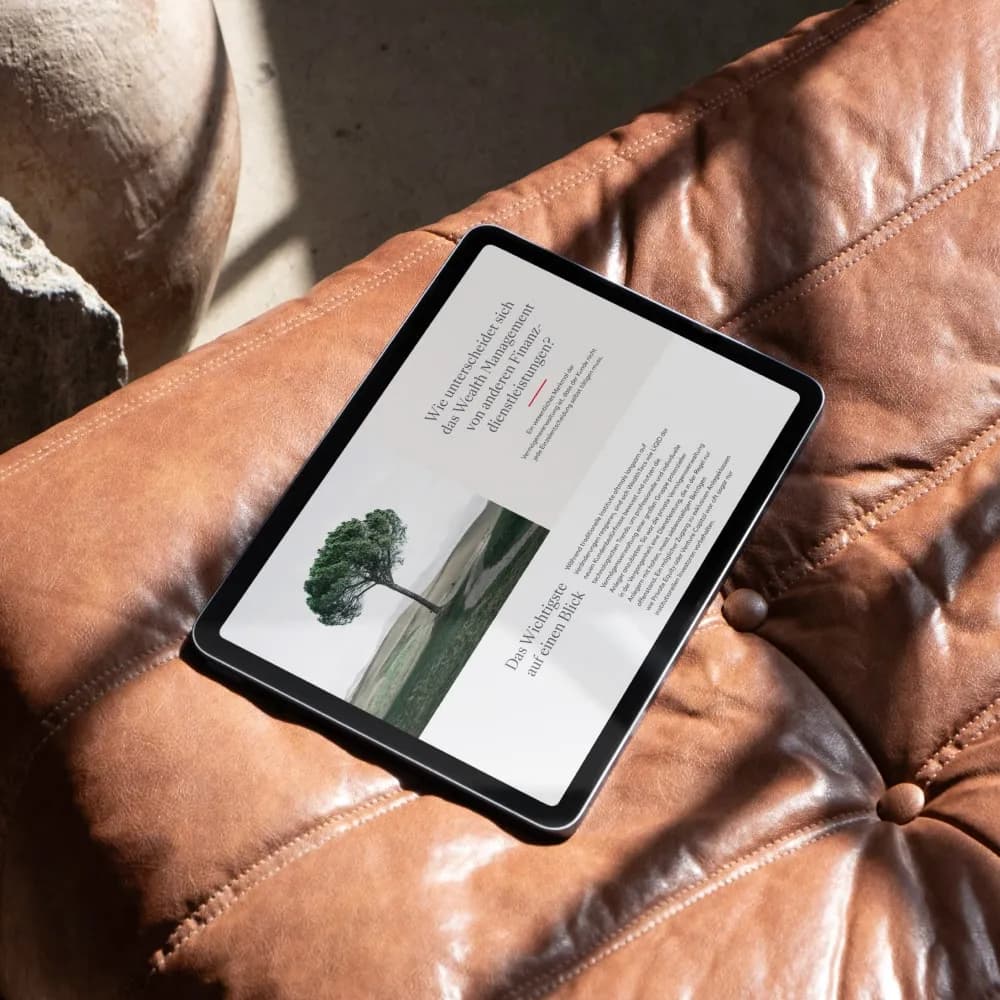 Tablet mit Textseite und Baum, auf braunem Ledersofa liegend