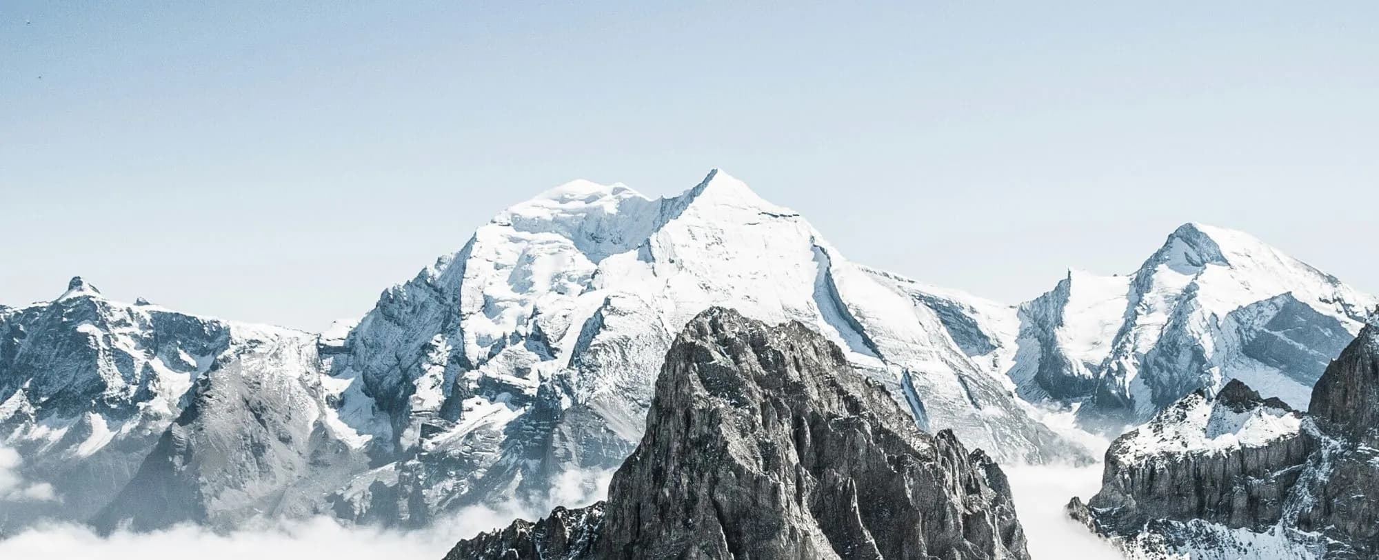 Verschneite Alpengipfel ragen über Wolken in klarem Winterhimmel
