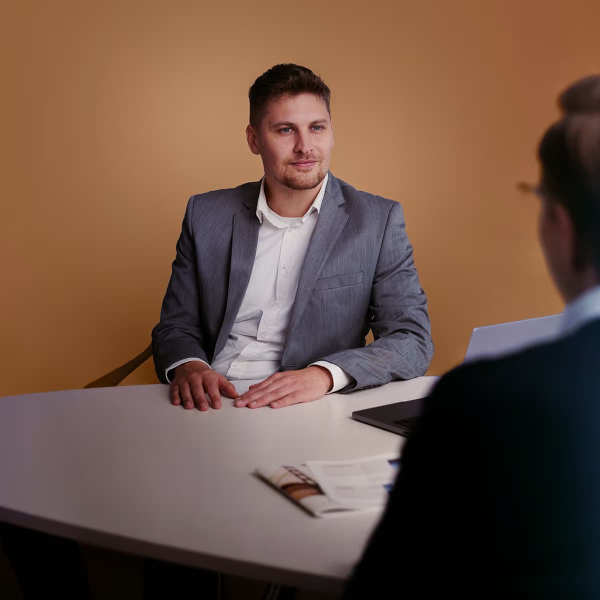 Geschäftsmann im grauen Anzug sitzt an einem Schreibtisch während eines Gesprächs