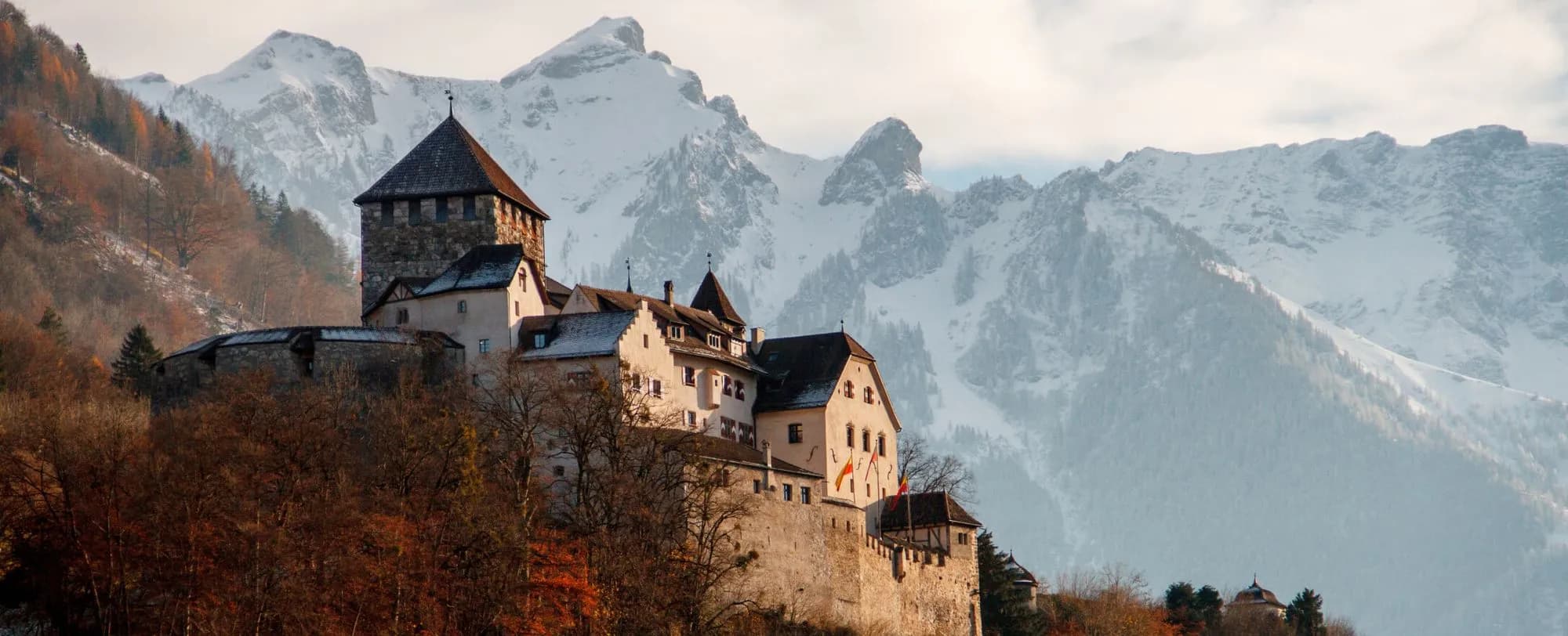 Historische Burg auf Felsen mit verschneiten Alpen im Hintergrund